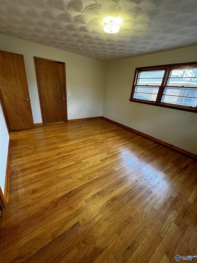 unfurnished bedroom featuring multiple closets, light hardwood / wood-style flooring, and a textured ceiling