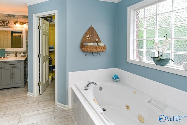 bathroom featuring baseboards, a tub with jets, crown molding, and vanity
