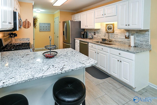 kitchen featuring a sink, stainless steel appliances, a kitchen bar, crown molding, and white cabinetry