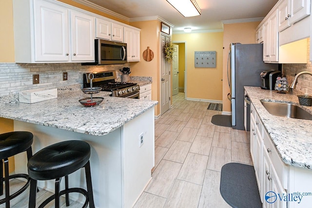kitchen with light stone counters, stainless steel appliances, backsplash, a sink, and white cabinetry