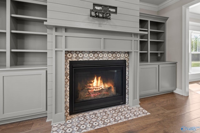 interior details featuring baseboards, built in features, a fireplace, crown molding, and wood finished floors