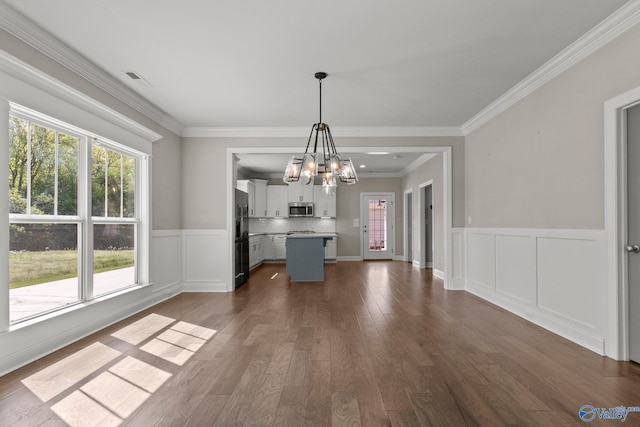 unfurnished dining area with ornamental molding, visible vents, a wainscoted wall, a chandelier, and dark wood-style flooring