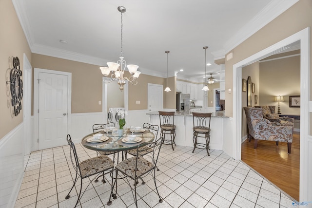 dining room with ceiling fan with notable chandelier, sink, ornamental molding, washer and clothes dryer, and light wood-type flooring