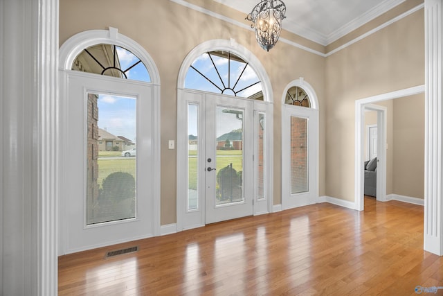 entryway with ornamental molding, light wood-type flooring, and a notable chandelier