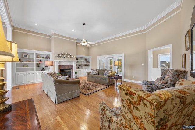 living room featuring a fireplace, light hardwood / wood-style floors, a towering ceiling, and crown molding