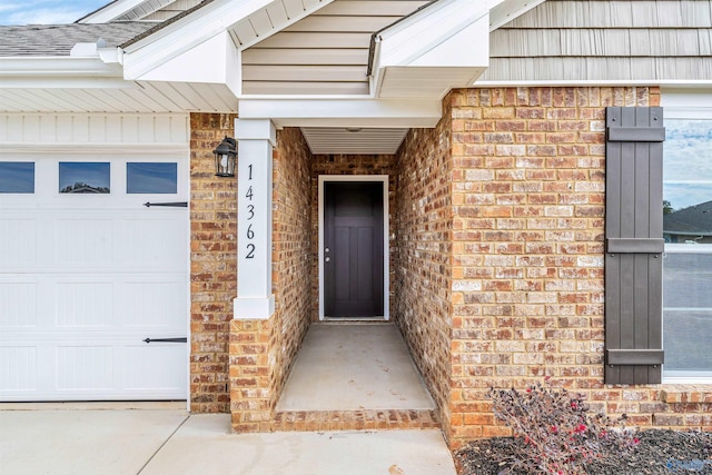 entrance to property featuring a garage, a shingled roof, and brick siding