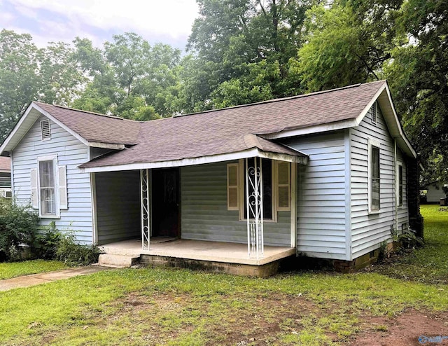 ranch-style home featuring roof with shingles, covered porch, and a front lawn