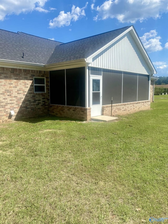 back of property featuring a sunroom, brick siding, a yard, and roof with shingles