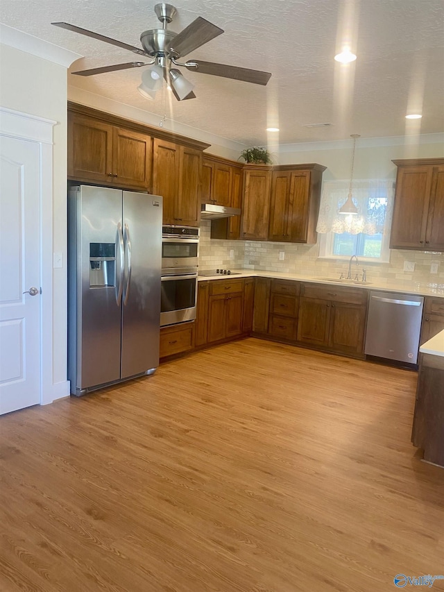 kitchen featuring decorative backsplash, appliances with stainless steel finishes, under cabinet range hood, light wood-style floors, and a sink