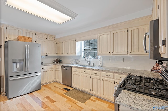 kitchen with light stone countertops, appliances with stainless steel finishes, tasteful backsplash, light hardwood / wood-style floors, and sink