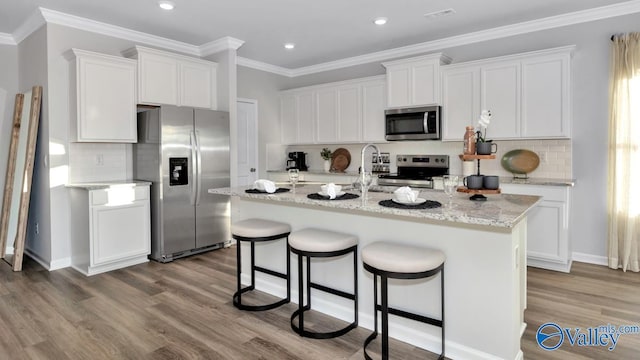 kitchen with white cabinets, ornamental molding, an island with sink, and appliances with stainless steel finishes