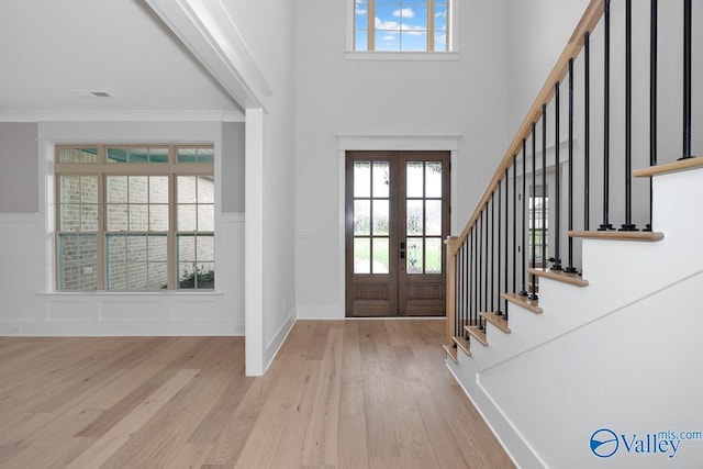 foyer entrance featuring a decorative wall, stairs, wood finished floors, a wainscoted wall, and french doors
