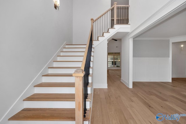 staircase with wood finished floors and ornamental molding