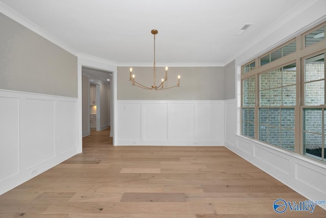 unfurnished dining area with a decorative wall, crown molding, wainscoting, light wood-style floors, and a notable chandelier
