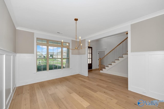 unfurnished dining area featuring light wood-type flooring, a wainscoted wall, a chandelier, and a decorative wall