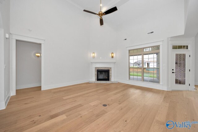 unfurnished living room with light wood-type flooring, ceiling fan, a fireplace, a high ceiling, and visible vents