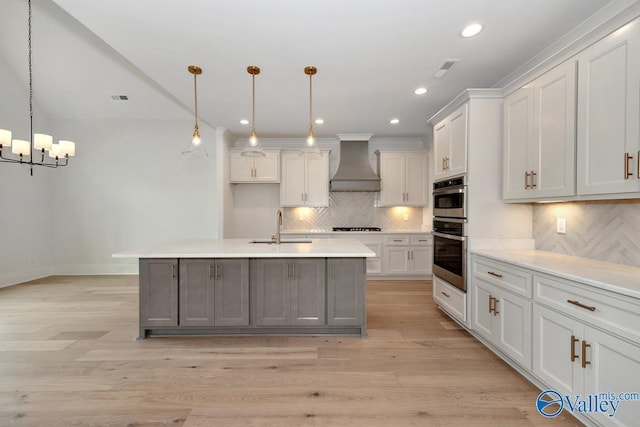 kitchen with backsplash, light countertops, a sink, premium range hood, and a notable chandelier