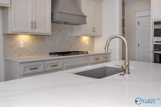 kitchen featuring backsplash, a sink, light stone countertops, appliances with stainless steel finishes, and custom exhaust hood