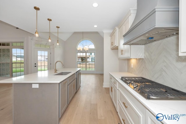 kitchen featuring vaulted ceiling, a sink, a chandelier, premium range hood, and appliances with stainless steel finishes