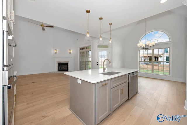 kitchen featuring light wood finished floors, a sink, gray cabinetry, a glass covered fireplace, and appliances with stainless steel finishes
