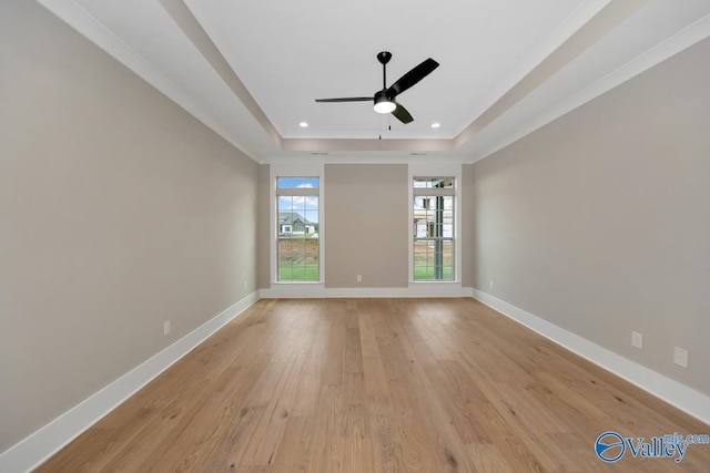 spare room with a tray ceiling, a ceiling fan, light wood-style floors, crown molding, and baseboards