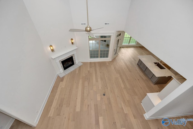 unfurnished living room with a towering ceiling, wood finished floors, baseboards, a tiled fireplace, and ceiling fan