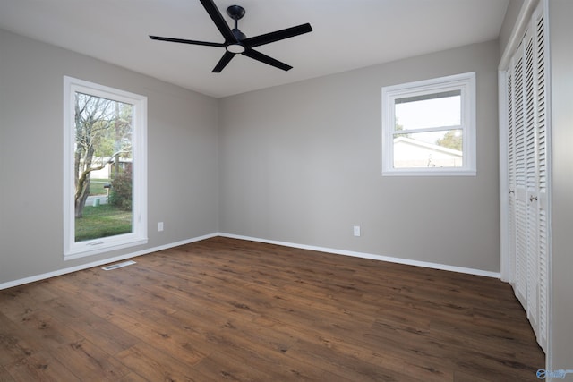 unfurnished bedroom with a closet, multiple windows, dark hardwood / wood-style floors, and ceiling fan