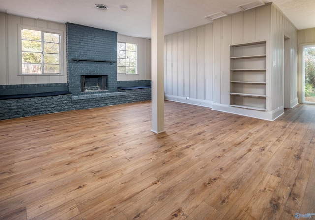 unfurnished living room featuring a brick fireplace, light hardwood / wood-style floors, and built in features