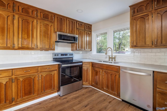 kitchen featuring appliances with stainless steel finishes, sink, tasteful backsplash, and light hardwood / wood-style flooring