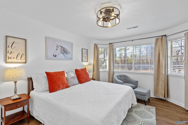 bedroom with multiple windows, wood finished floors, visible vents, and baseboards