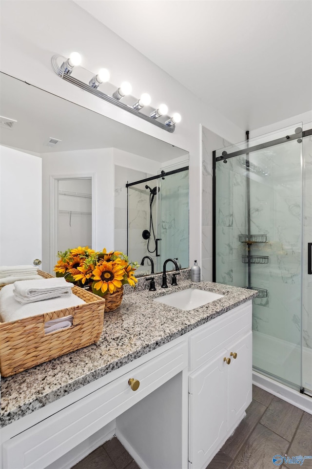 bathroom with vanity, wood finished floors, visible vents, and a marble finish shower