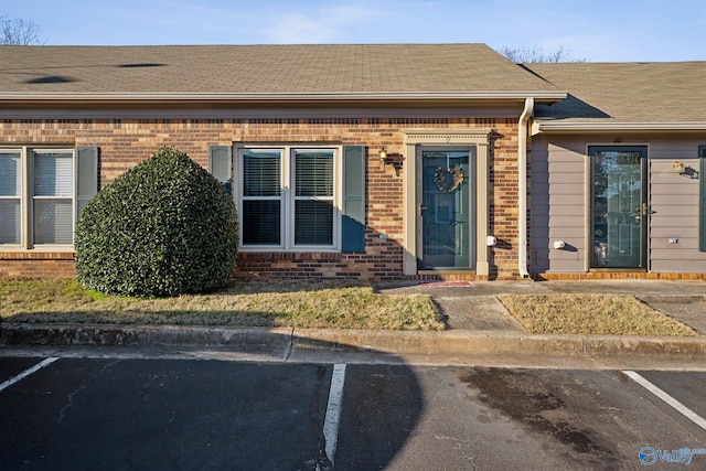 doorway to property featuring uncovered parking, brick siding, and a shingled roof