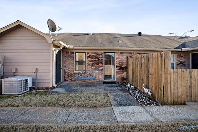 rear view of house featuring a shingled roof, cooling unit, brick siding, and fence