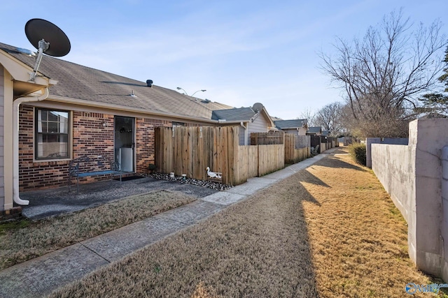 view of home's exterior featuring brick siding, fence, and roof with shingles