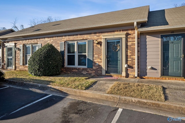 view of front of property featuring roof with shingles, uncovered parking, and brick siding