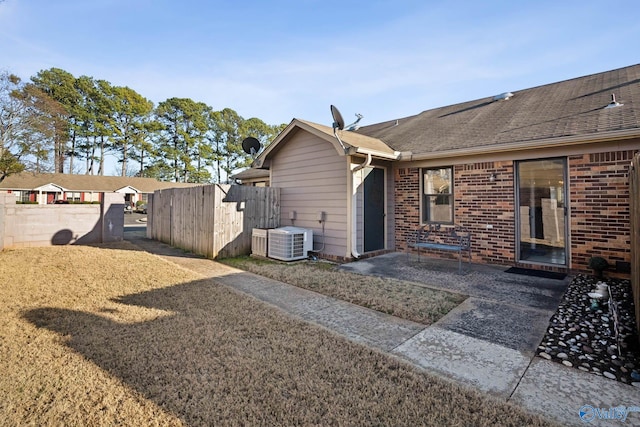rear view of property with brick siding, a shingled roof, central AC unit, a patio area, and fence