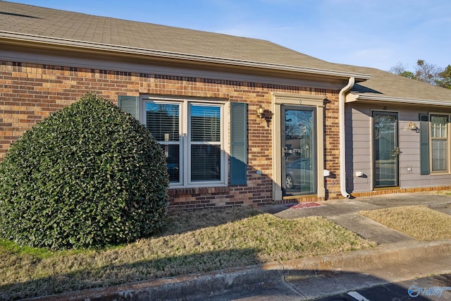 view of exterior entry with brick siding and roof with shingles