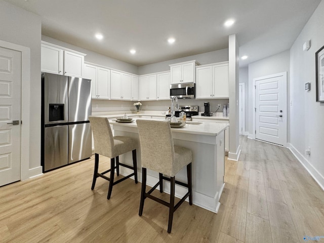 kitchen with appliances with stainless steel finishes, a kitchen breakfast bar, light hardwood / wood-style floors, white cabinetry, and an island with sink