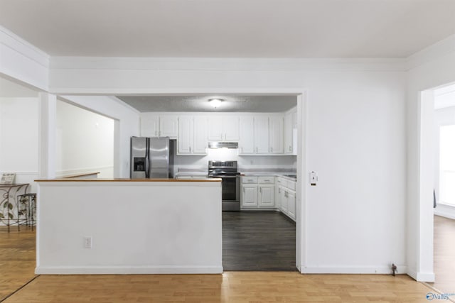 kitchen with appliances with stainless steel finishes, white cabinetry, ornamental molding, kitchen peninsula, and light wood-type flooring