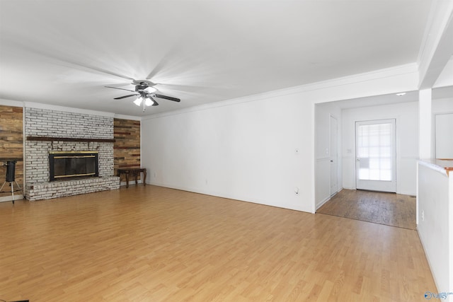 unfurnished living room with ceiling fan, a brick fireplace, crown molding, and light wood-type flooring