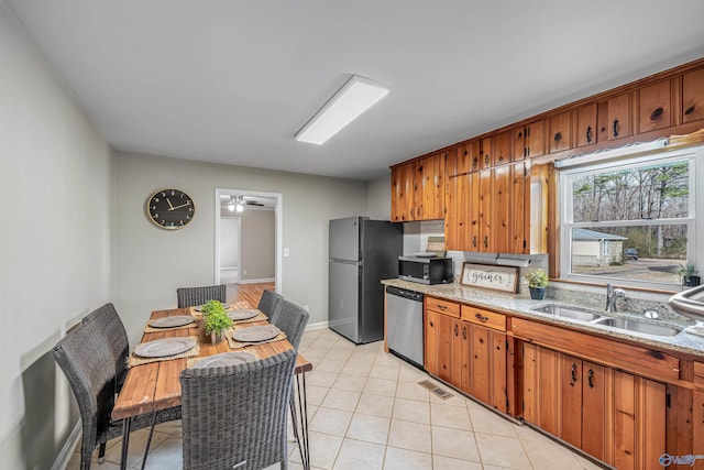 kitchen featuring sink, light tile patterned floors, ceiling fan, stainless steel appliances, and light stone countertops