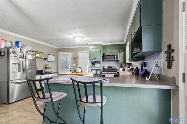 kitchen featuring stainless steel appliances, a kitchen breakfast bar, kitchen peninsula, crown molding, and green cabinetry