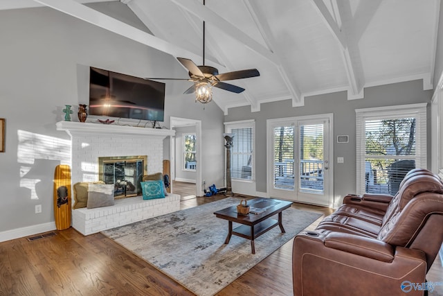 living room featuring a fireplace, wood-type flooring, vaulted ceiling with beams, and ceiling fan