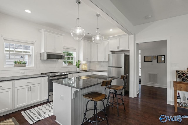 kitchen featuring stainless steel appliances, backsplash, white cabinetry, dark wood-type flooring, and a kitchen breakfast bar