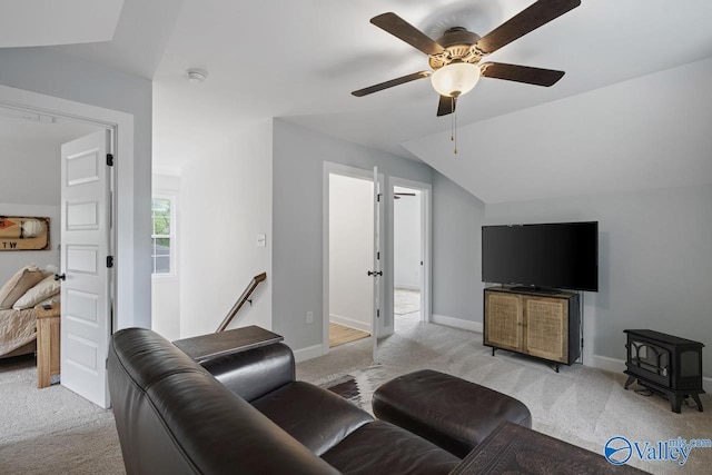 living area with light colored carpet, a wood stove, vaulted ceiling, a ceiling fan, and baseboards