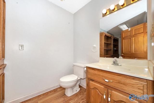 bathroom with toilet, wood finished floors, vanity, and baseboards