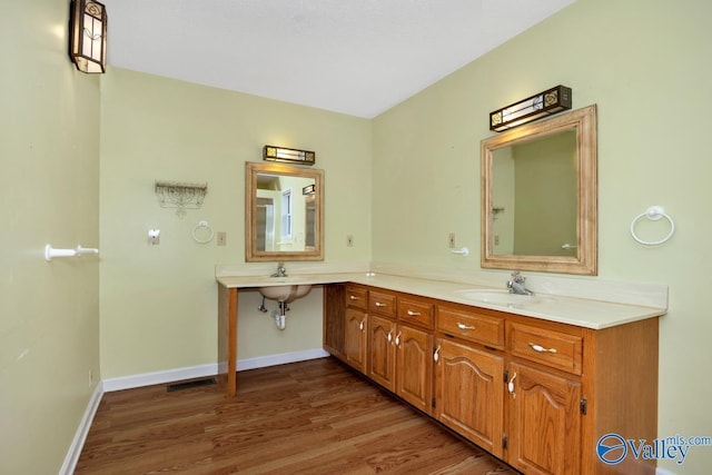 bathroom featuring baseboards, double vanity, visible vents, a sink, and wood finished floors
