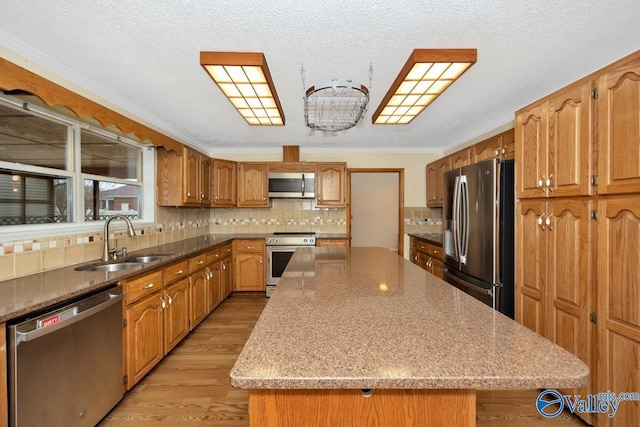 kitchen featuring appliances with stainless steel finishes, a kitchen island, decorative backsplash, light wood finished floors, and a sink