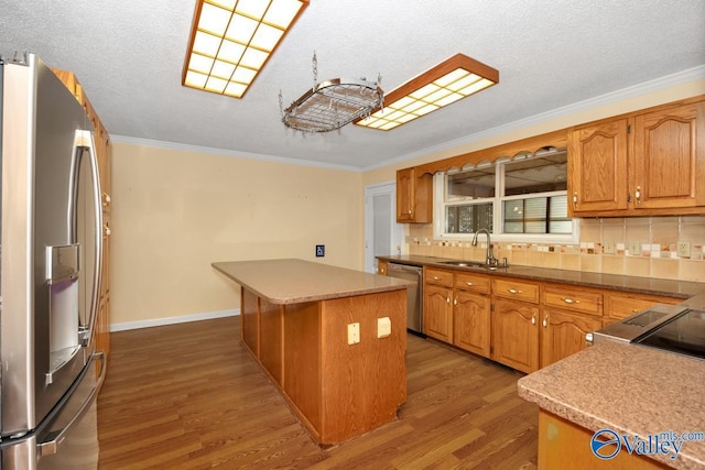 kitchen featuring crown molding, a center island, wood finished floors, a sink, and stainless steel appliances