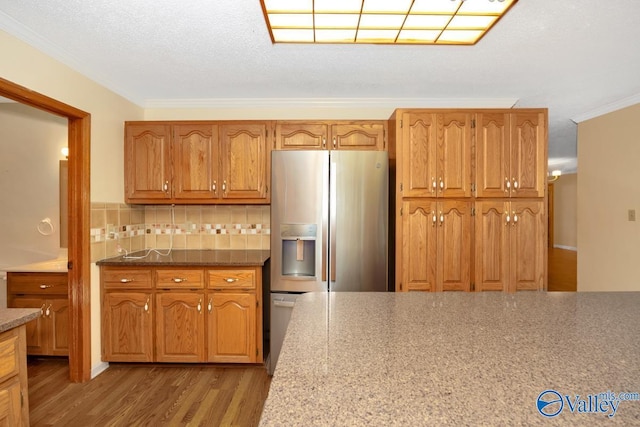 kitchen with crown molding, stainless steel refrigerator with ice dispenser, wood finished floors, brown cabinets, and decorative backsplash